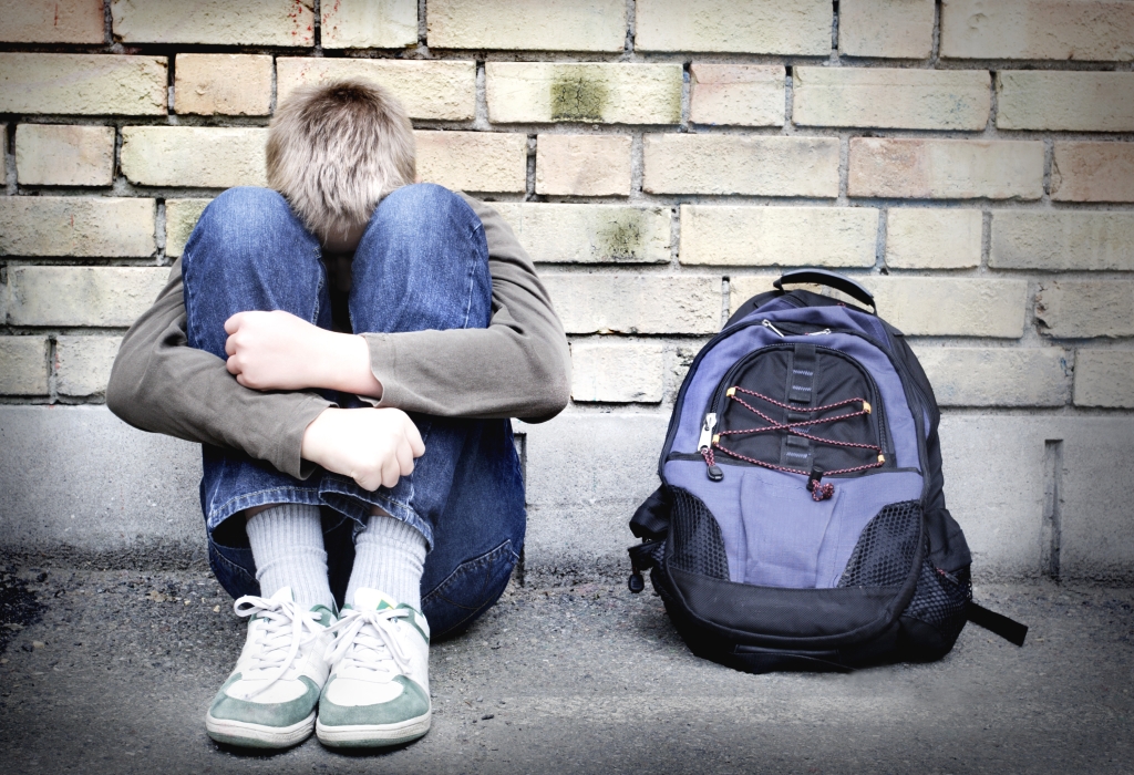 Young vulnerable child hiding his head hugging his knees while sitting on the street.