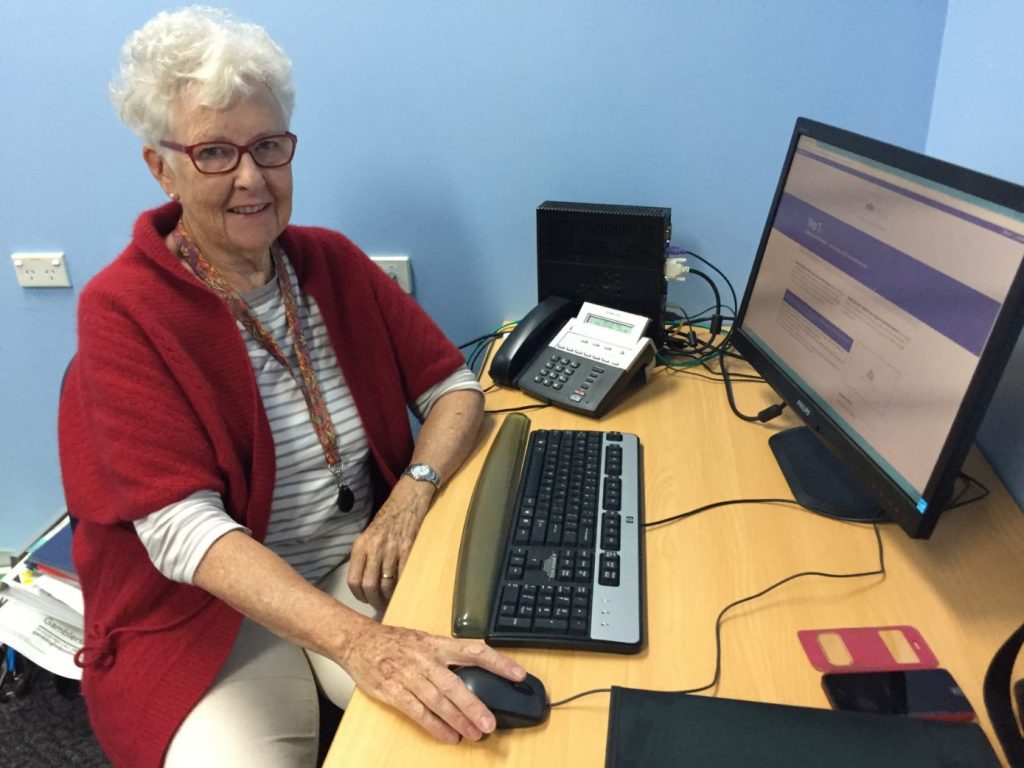 Volunteer financial counsellor sitting in front of computer smiling