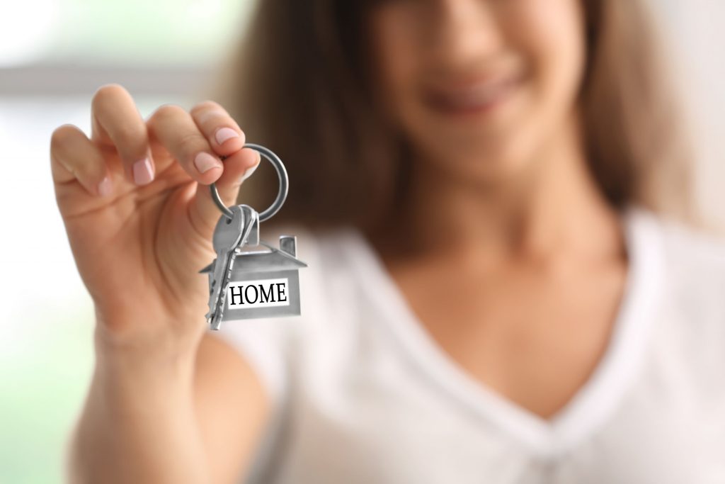 Someone holding out a set of keys with a key ring which has a key charm the shape of a house with the words HOME on it.
