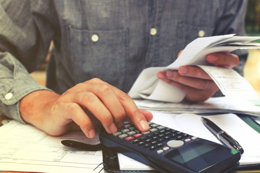 person using their phone as a calculator holding a stack of receipts indicating concern over money