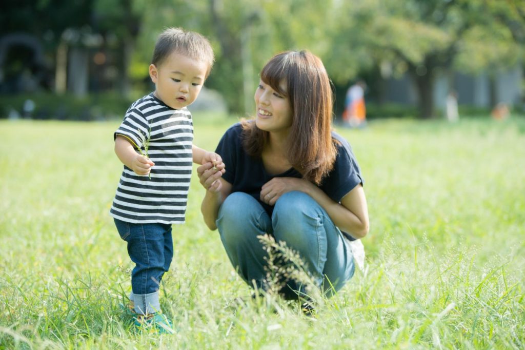 A mother squatting beside a child on a lawn