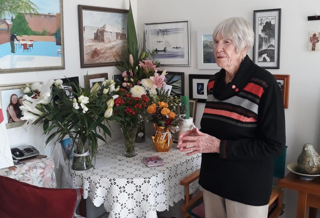 Anglicare Tasmania home care client Agnes is standing next to her collection of flowers received in celebration of her 100th birthday