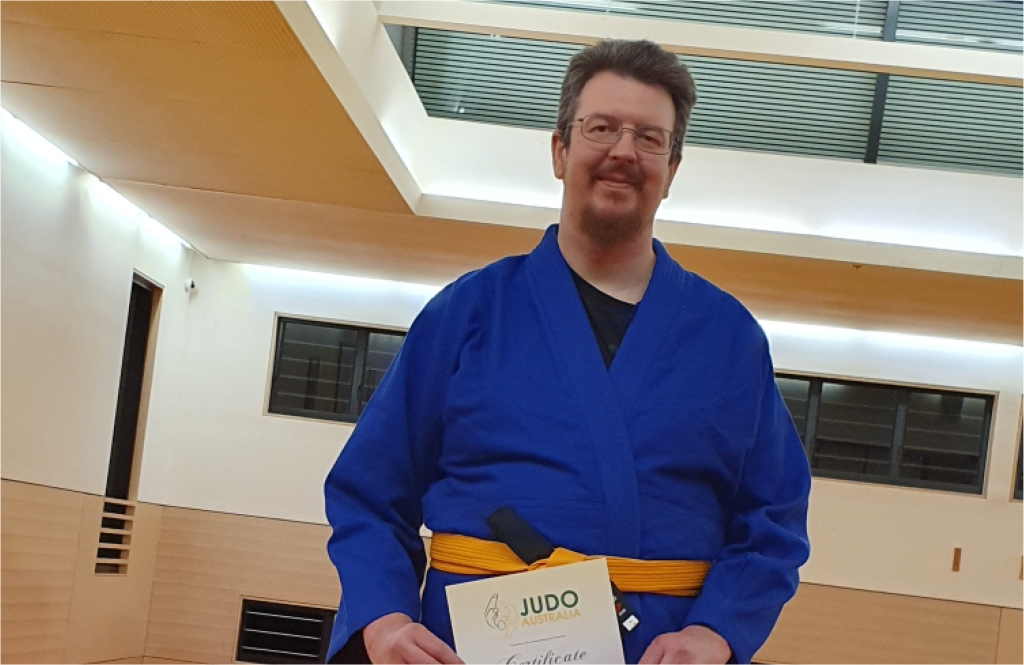 Photo of Anglicare's Acquired Injury Support Services client Matthew wearing his gi and holding his certificate of achivement