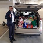 Photo of Mark Holland, chaplain from The Hutchins School standing next to the boot of his car. It is open and full of items.