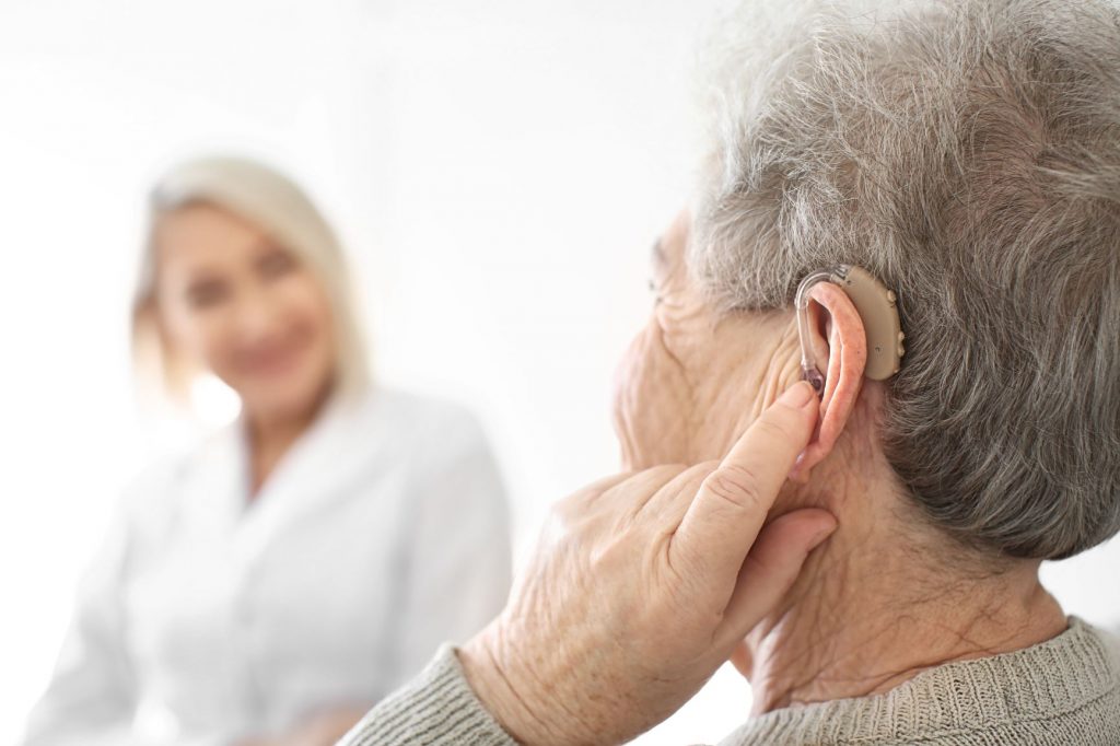 The side of someone's head. They are touching their ear which has a hearing aid in it.
