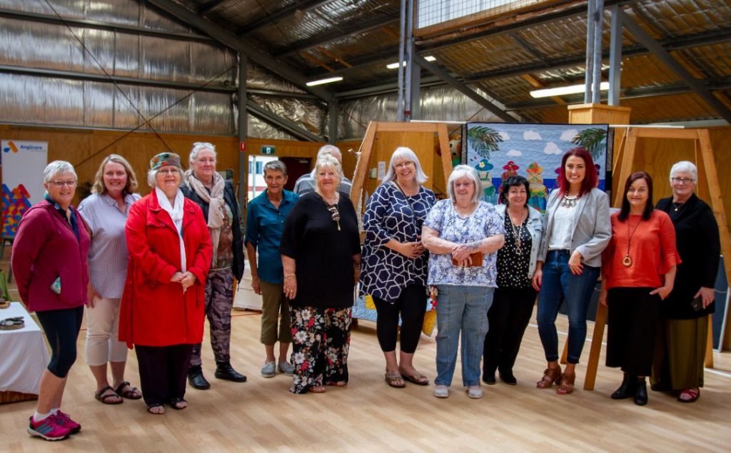 A group of women standing together for a photo. There is a collection of artwork in the background.