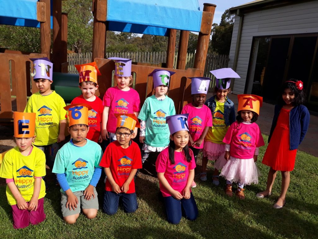 A group of children graduating from the HIPPY kids program in Launceston. They are wearing Hippy Australia t-shirts of different colours and a carboard hat with a letter or number on them.