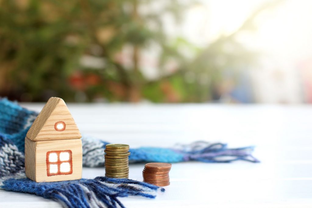 a small wooden toy that looks like a house. Sitting on a woolly winter scarf. Piles of coins sitting beside them.