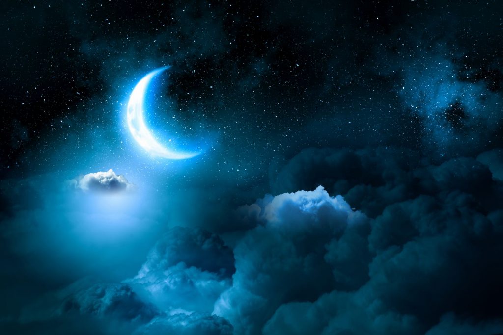night sky with a wedge of the moon shining bright. Clouds in the night sky with stars in the background.