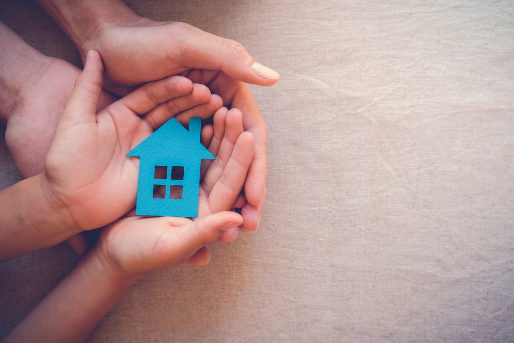 an image of a small pair of hands holding a blue house cut out and their hands are resting in some adult hands.