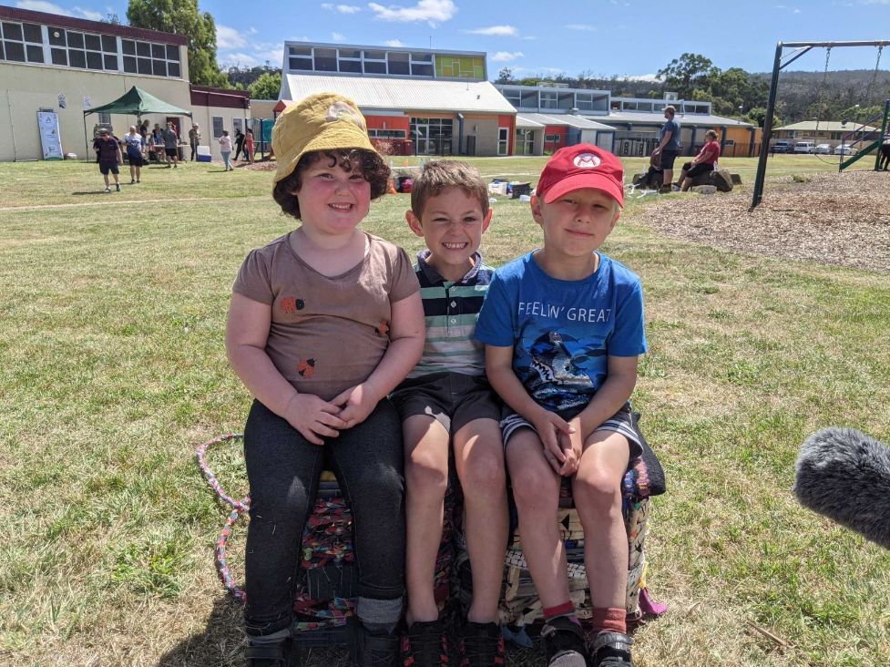 Three children sitting in the playground together in the sun with the hats on.