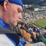 Garry is sitting in a football stadium.
