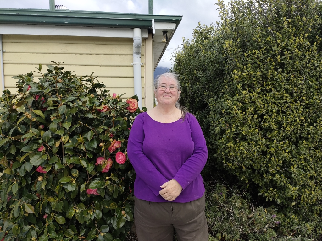 Barb Phillips standing in a garden beside a house smiling.