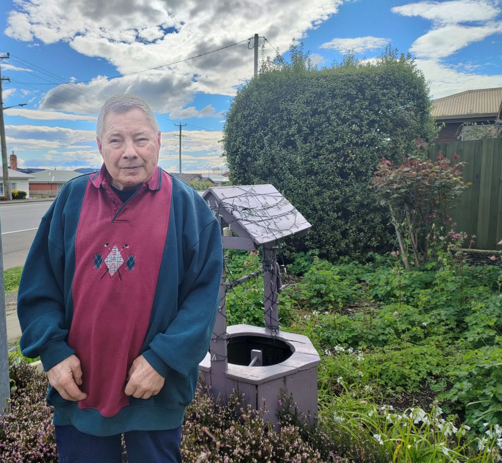 George standing in a garden in front of the wishing well that he made.