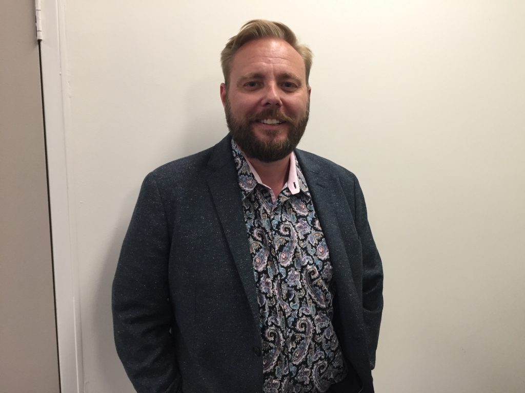 man with paisley shirt and a jacket, a beard smiling