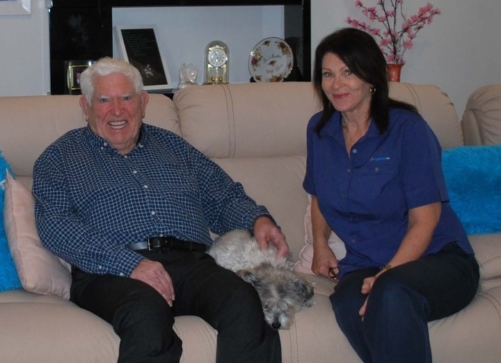 Anglicare Home Care Support Worker sitting on the couch with a client and their dog.