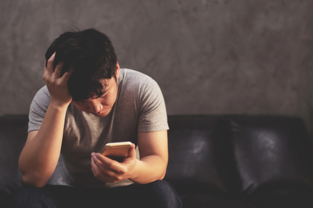 How does Gambling Harm affect others? Pictured: Young man looks despondently at the mobile phone in his hand