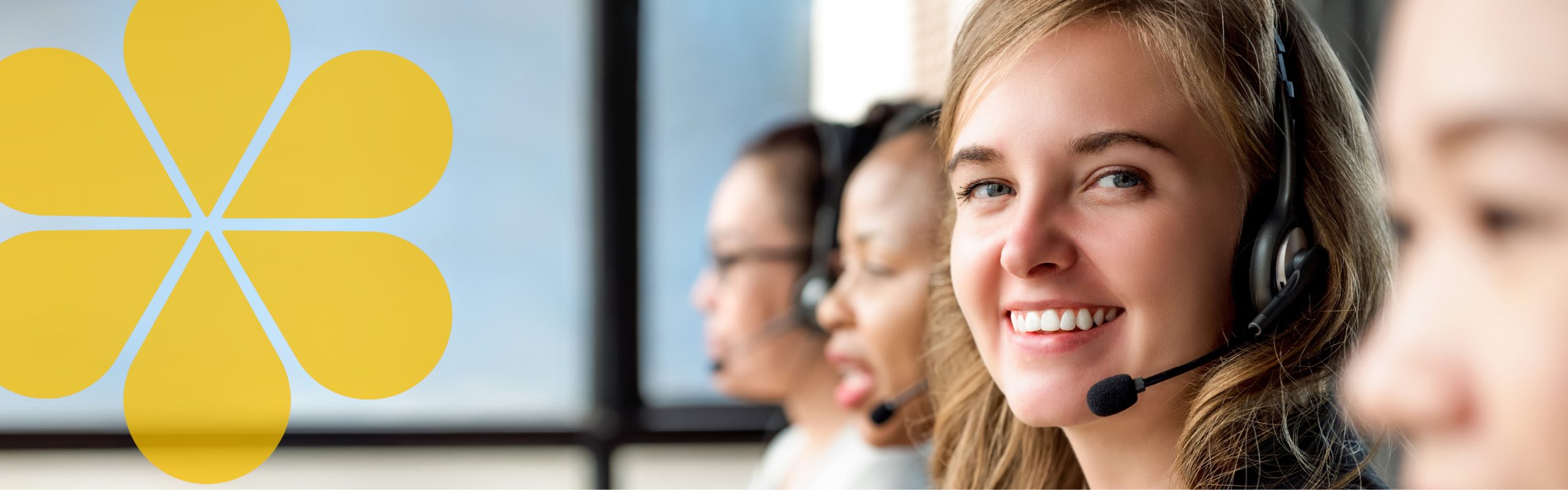 People with headsets and smiling. They appear to be talking on the phone. One person is looking at the camera and smiling.