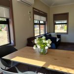 Lounge and dining area with a modern timber topped table and chairs, a couple of lounge chairs and lots of windows and views of the garden.