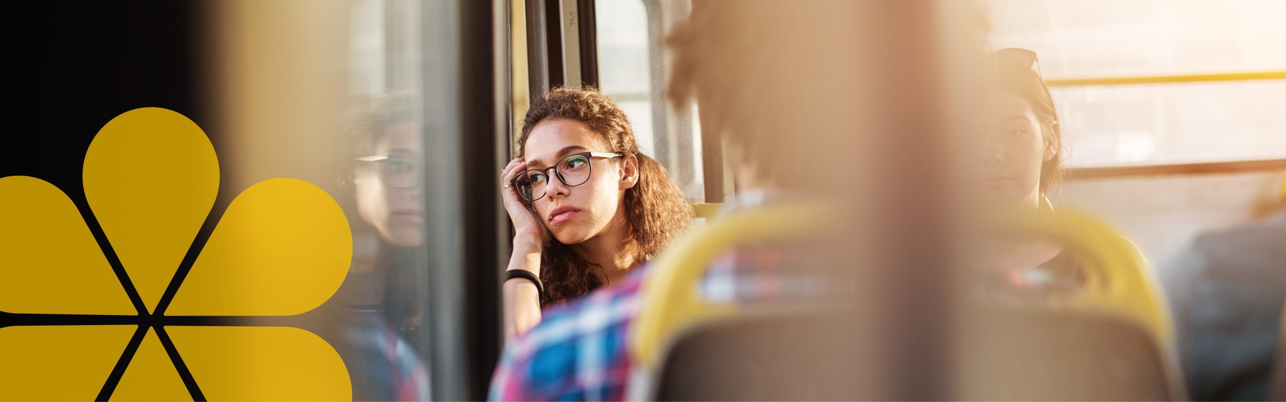 A young woman contemplatively looking out a window she is leaning on while riding the bus.