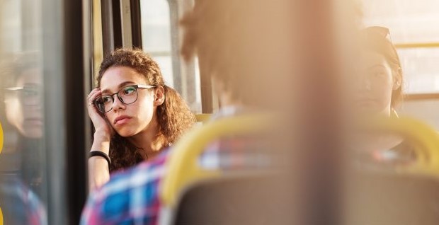 Image of a person sitting on a bus with their head against the window looking out the window.