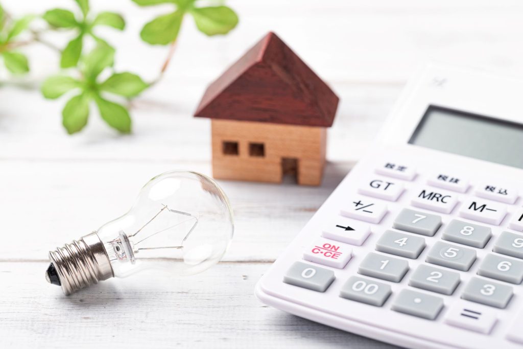 A calculator sitting on atable next to a lightbulb and a small timber model of a house.