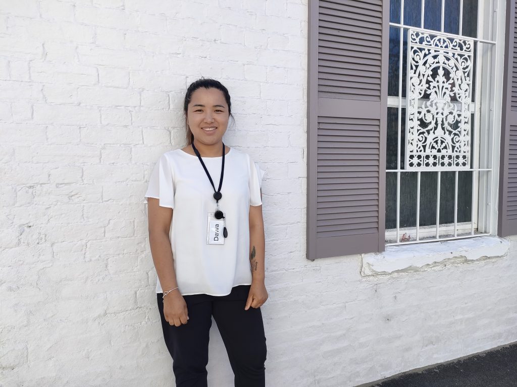 A photo of Dawa leaning against a brick wall. She is smiling.