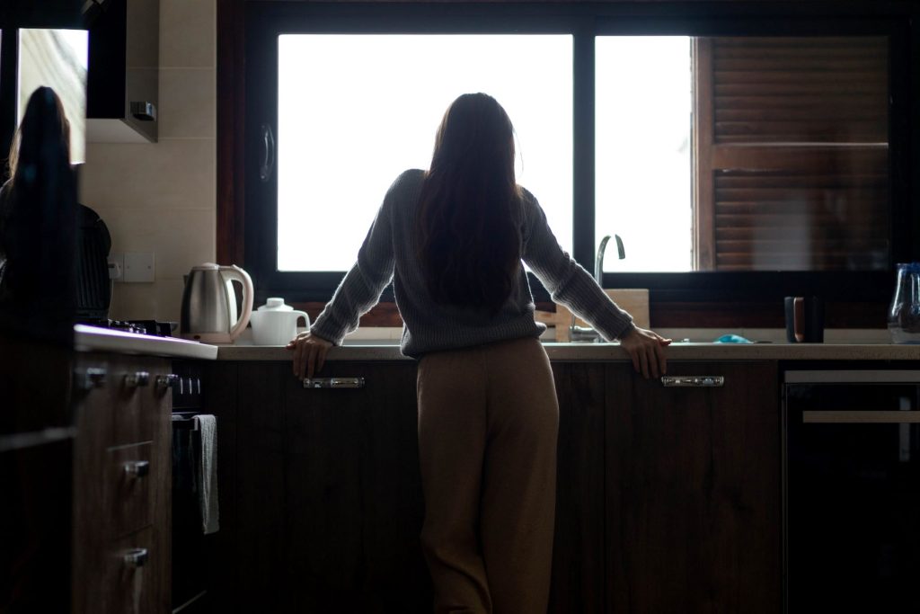 The back of a person who is looking out of the window in their kitchen.