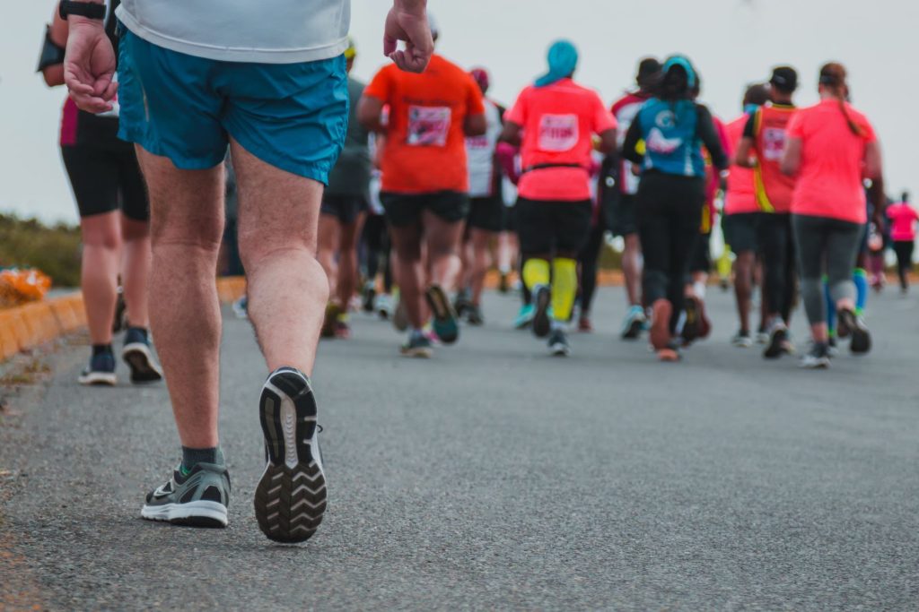 A photo of the back of a group of people running and their is one runner that is being left behind.