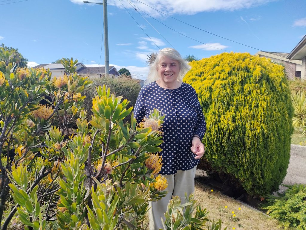 Judy Cornwell is standing in her home garden smiling.