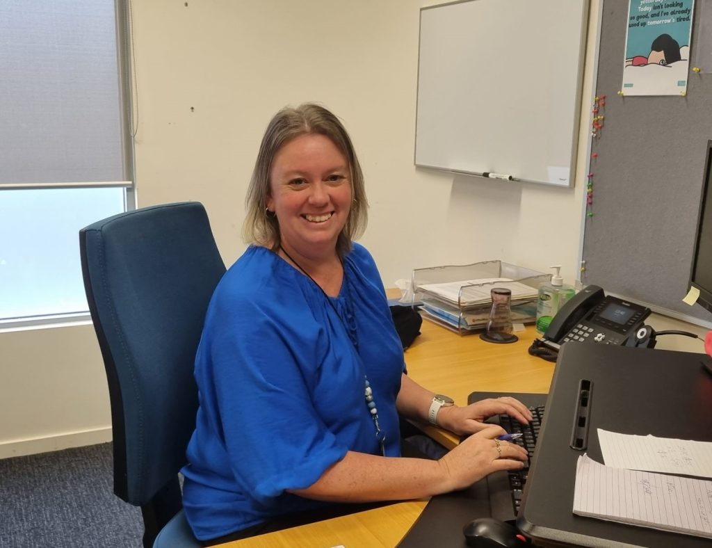 Jodie sitting at her desk in front of the computer, smiling at the camera