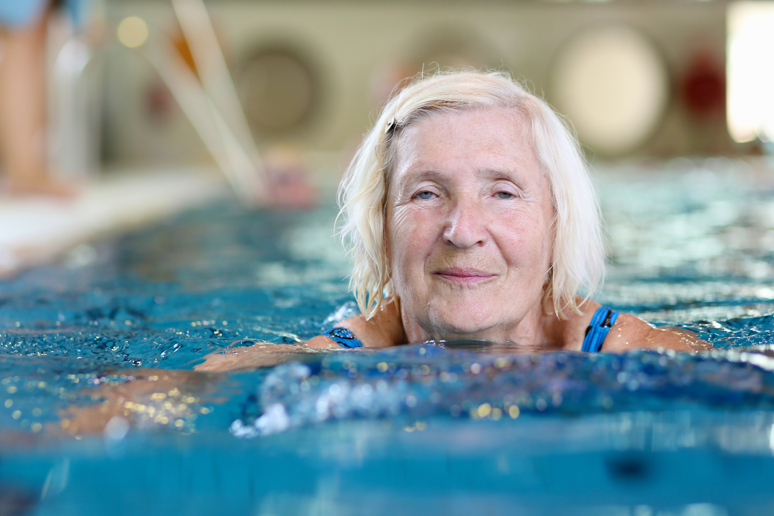 An older person is swimming in a pool and looks happy.