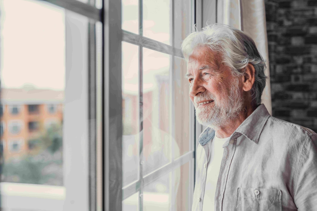 A photo of a man looking through a window. He is smiling.